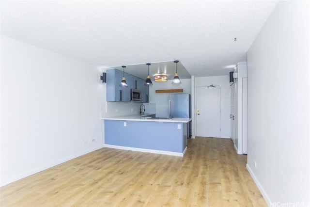 kitchen with light wood finished floors, a peninsula, a sink, light countertops, and appliances with stainless steel finishes