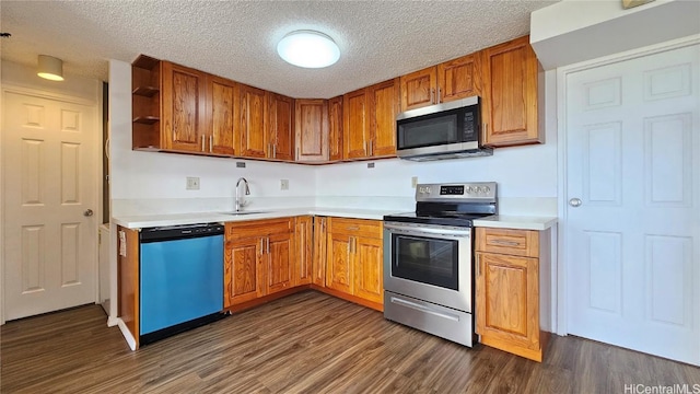 kitchen with brown cabinets, a sink, appliances with stainless steel finishes, light countertops, and dark wood-style flooring