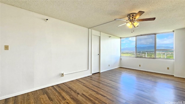 empty room with wood finished floors, baseboards, ceiling fan, a textured ceiling, and a mountain view