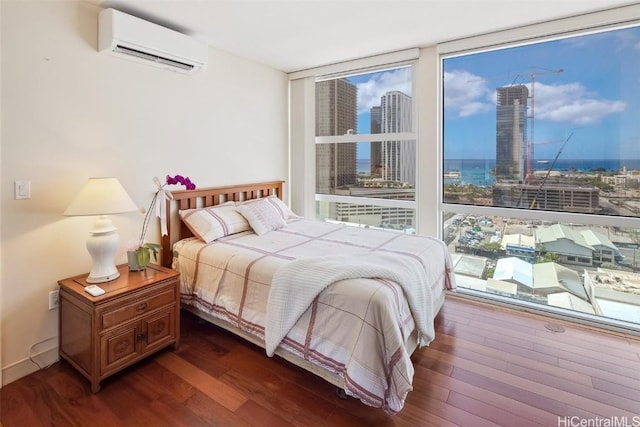 bedroom with a city view, dark wood-style floors, a wall mounted air conditioner, and expansive windows