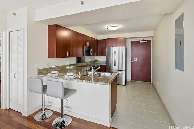 kitchen with a kitchen bar, a sink, stainless steel appliances, a peninsula, and baseboards