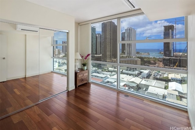 unfurnished bedroom featuring a wall mounted air conditioner, a city view, wood finished floors, a closet, and a wall of windows