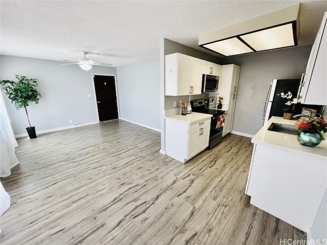 kitchen featuring light wood-type flooring, range with electric cooktop, stainless steel microwave, light countertops, and ceiling fan