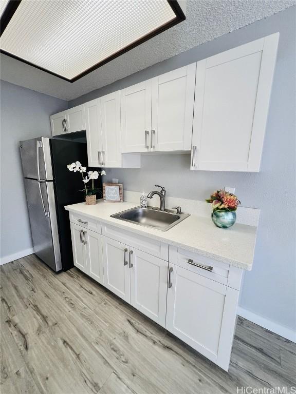 kitchen featuring light countertops, white cabinets, freestanding refrigerator, and a sink