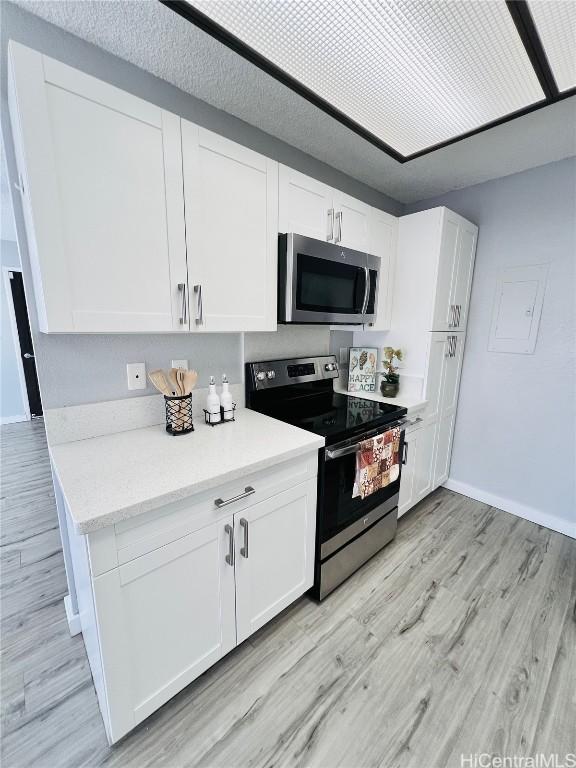 kitchen with white cabinetry, appliances with stainless steel finishes, light wood finished floors, baseboards, and light stone countertops