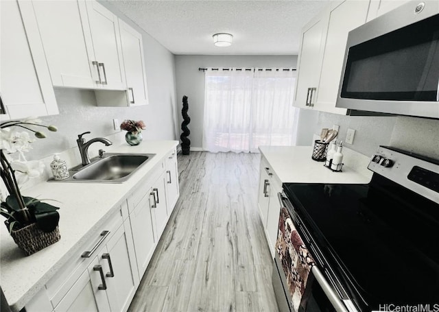 kitchen with a sink, stainless steel appliances, white cabinets, light wood-style floors, and a textured ceiling