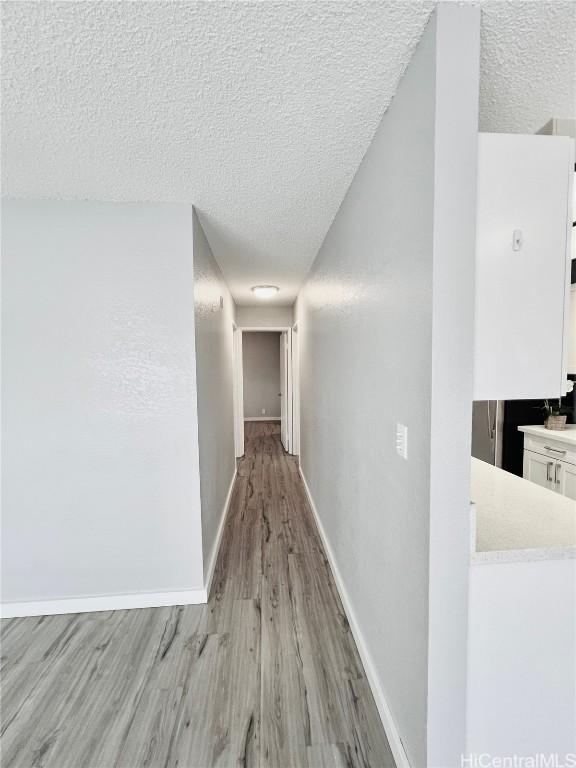 corridor with baseboards, light wood-type flooring, and a textured ceiling