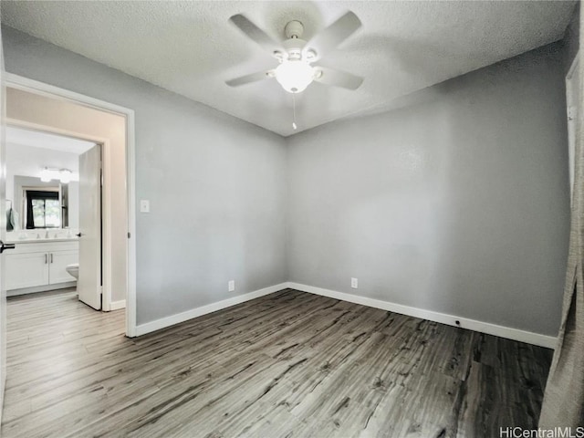 unfurnished bedroom featuring baseboards, a textured ceiling, wood finished floors, and ensuite bathroom