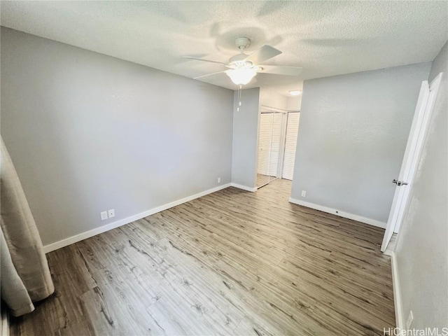 unfurnished bedroom with a closet, a textured ceiling, baseboards, and wood finished floors