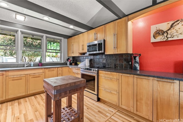 kitchen with beam ceiling, light wood-style flooring, a sink, stainless steel appliances, and backsplash