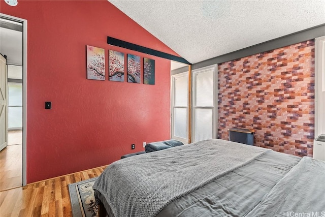 bedroom with a textured ceiling, wood finished floors, and vaulted ceiling