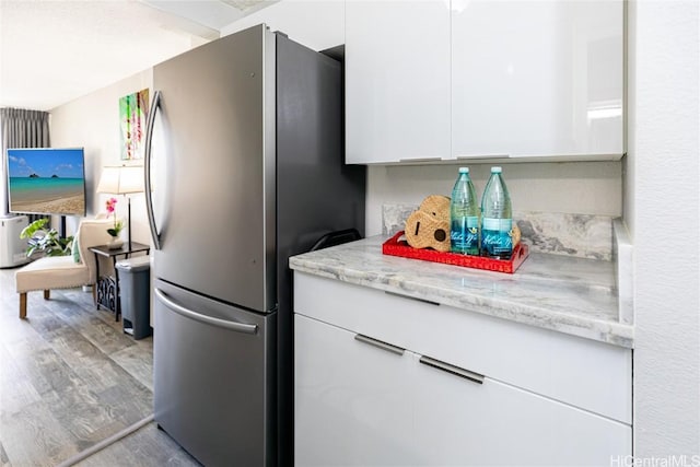 kitchen featuring modern cabinets, light wood-style flooring, light stone counters, white cabinetry, and freestanding refrigerator