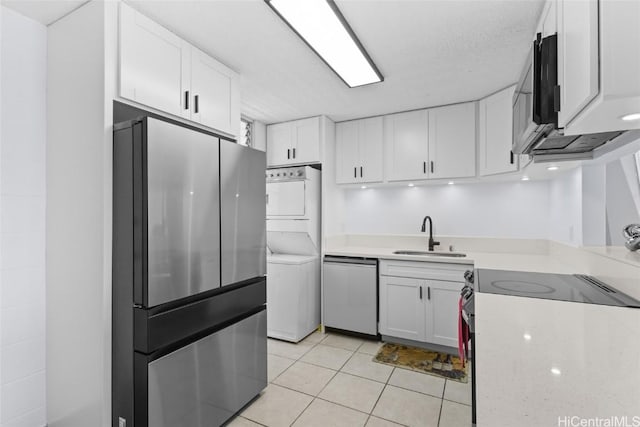 kitchen featuring a sink, light countertops, stacked washer / drying machine, appliances with stainless steel finishes, and white cabinetry