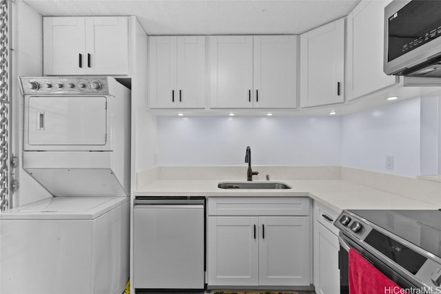 kitchen featuring stacked washer and dryer, a sink, white cabinetry, appliances with stainless steel finishes, and light countertops