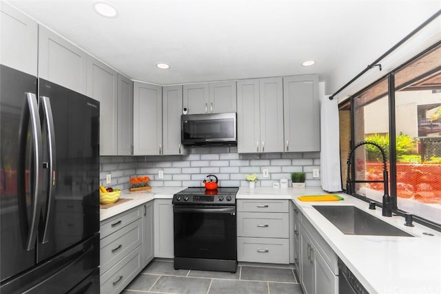 kitchen featuring electric range oven, decorative backsplash, gray cabinets, freestanding refrigerator, and a sink