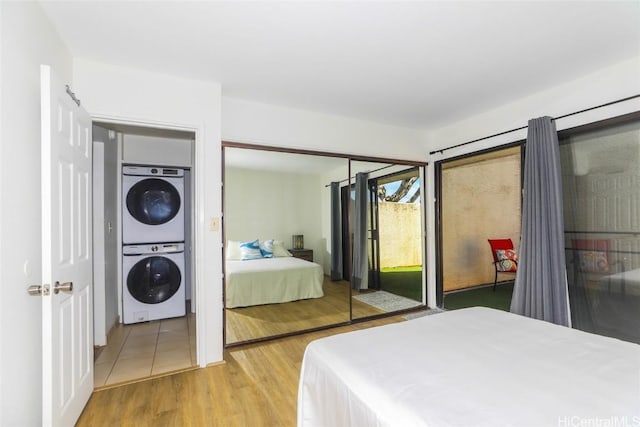 bedroom with access to exterior, wood finished floors, and stacked washer and clothes dryer