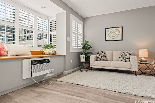 living area with a wall unit AC, wood finished floors, and baseboards