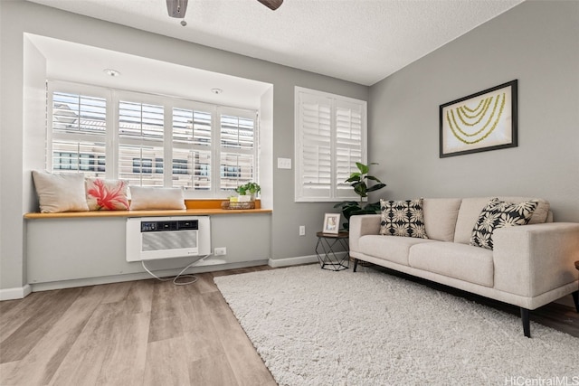 sitting room featuring wood finished floors, baseboards, a wall mounted AC, ceiling fan, and a textured ceiling