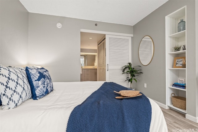 bedroom featuring connected bathroom, a closet, baseboards, and wood finished floors