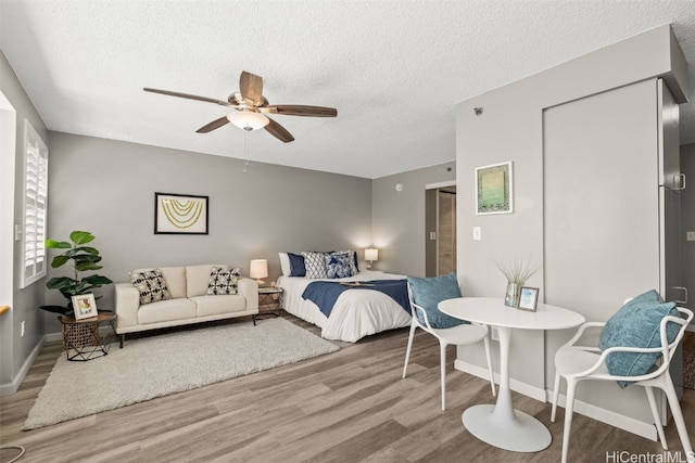 bedroom featuring baseboards, a textured ceiling, ceiling fan, and wood finished floors