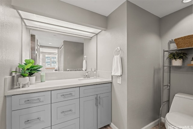 bathroom featuring baseboards, toilet, vanity, and a textured wall