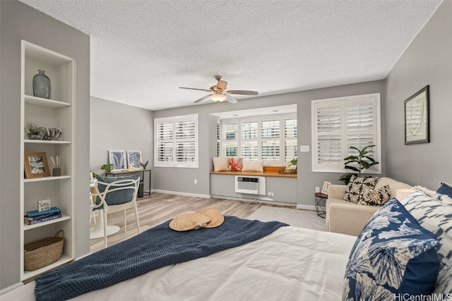 bedroom featuring baseboards, a textured ceiling, a wall unit AC, and wood finished floors