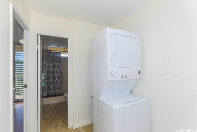 laundry area featuring concrete block wall, stacked washer and dryer, and laundry area