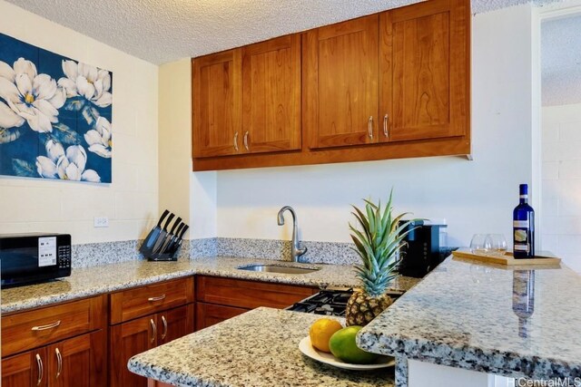 kitchen with a sink, a textured ceiling, brown cabinetry, and black microwave