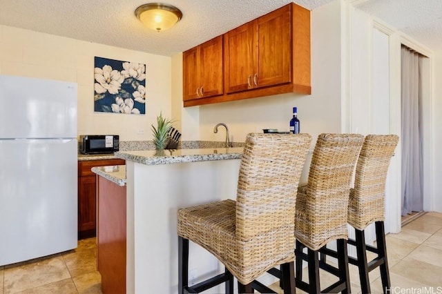 kitchen featuring black microwave, light tile patterned floors, a peninsula, freestanding refrigerator, and a textured ceiling