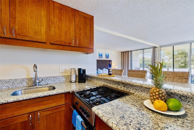 kitchen with brown cabinetry, light stone countertops, stainless steel gas range, a sink, and a textured ceiling