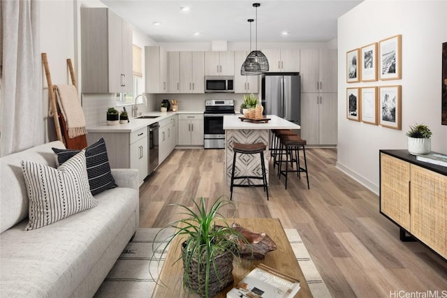 kitchen featuring light wood-style flooring, a sink, light countertops, appliances with stainless steel finishes, and a kitchen breakfast bar