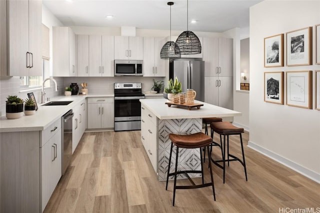 kitchen featuring a kitchen island, a sink, stainless steel appliances, light countertops, and a kitchen bar