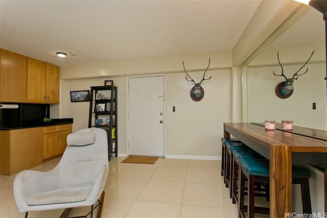 kitchen featuring light tile patterned floors, dark countertops, brown cabinetry, and baseboards