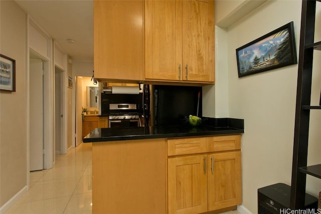 kitchen with light tile patterned floors, a peninsula, under cabinet range hood, dark countertops, and stainless steel gas stove