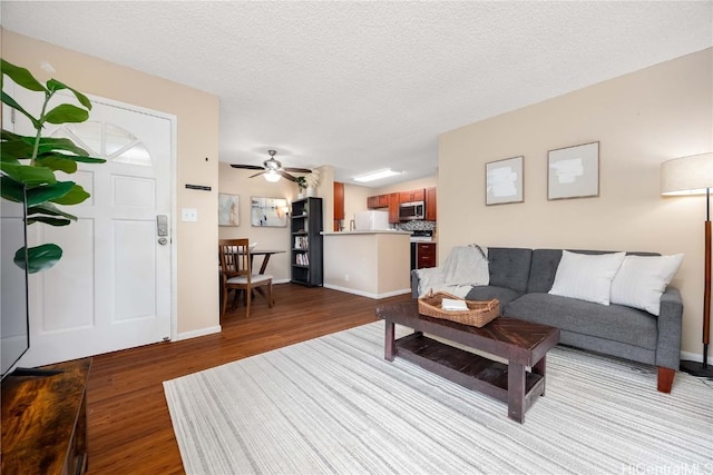 living area with ceiling fan, baseboards, a textured ceiling, and wood finished floors