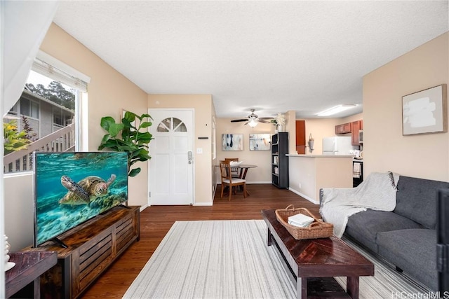 living area with dark wood-style floors, ceiling fan, and baseboards