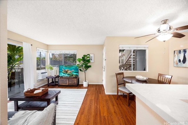 living room featuring cooling unit, a textured ceiling, baseboards, and wood finished floors