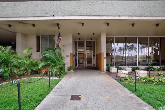 view of exterior entry with stucco siding and a yard