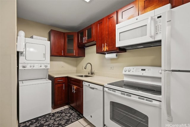 kitchen with white appliances, a sink, light countertops, stacked washer / dryer, and reddish brown cabinets