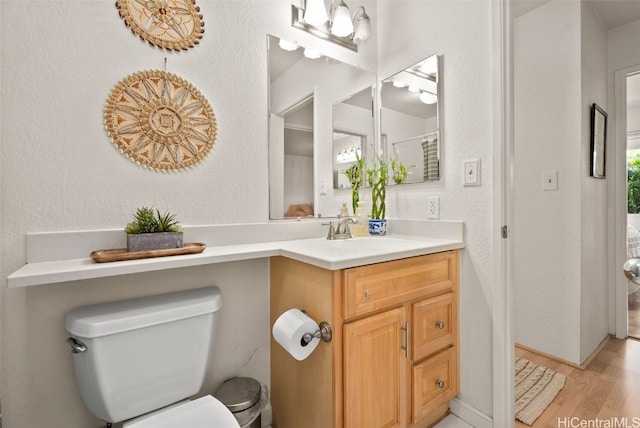 bathroom with toilet, vanity, a textured wall, and wood finished floors