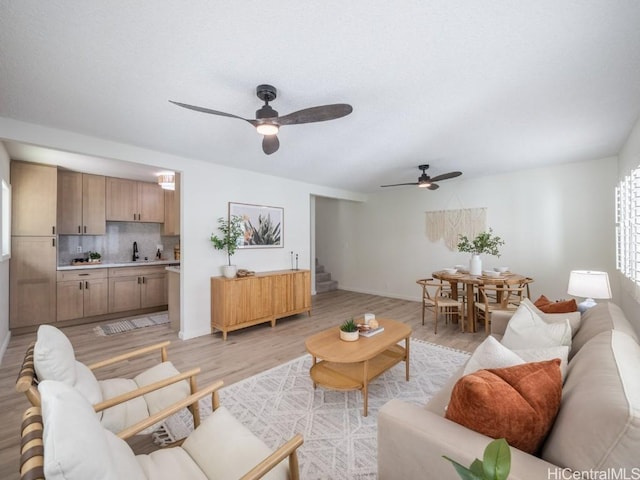 living area featuring stairway, light wood-style floors, and ceiling fan