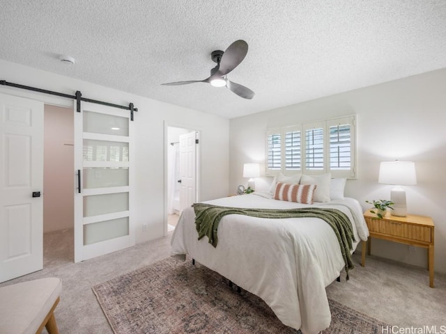 carpeted bedroom featuring ensuite bath, ceiling fan, a textured ceiling, and a barn door