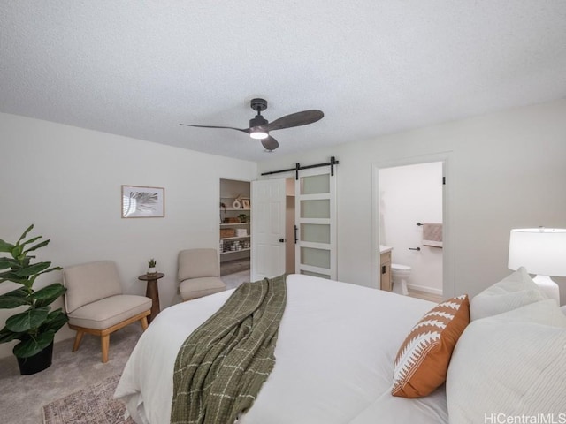 bedroom featuring ensuite bathroom, a ceiling fan, a textured ceiling, a barn door, and carpet flooring