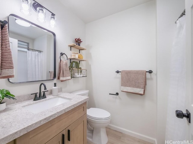 bathroom with baseboards, toilet, wood finished floors, and vanity