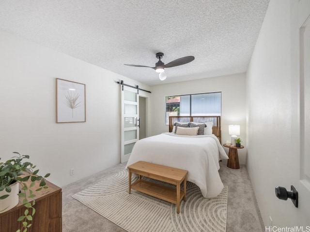 bedroom featuring ceiling fan, a barn door, light colored carpet, and a textured ceiling