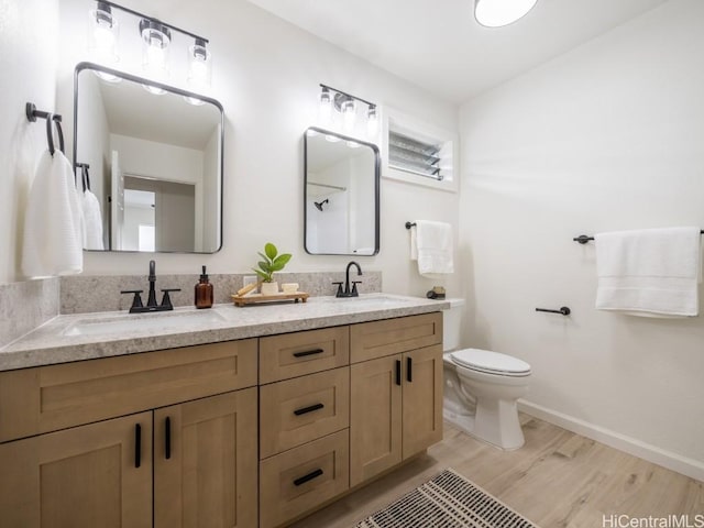 bathroom featuring double vanity, wood finished floors, toilet, and a sink