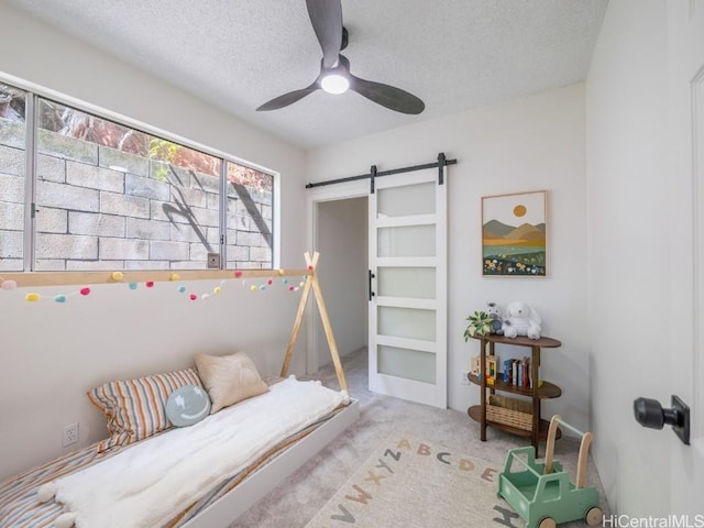 bedroom with a barn door, a textured ceiling, carpet flooring, and a ceiling fan