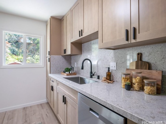 kitchen featuring backsplash, light stone counters, stainless steel dishwasher, light wood-style floors, and a sink