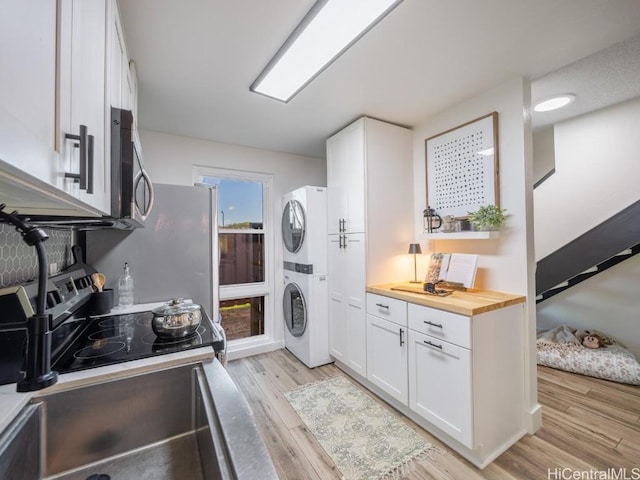 clothes washing area with a sink, light wood-style floors, stacked washer and clothes dryer, and laundry area