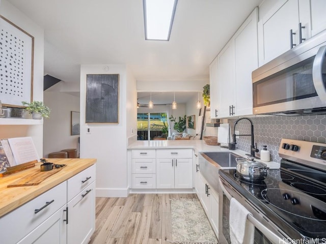 kitchen with a sink, backsplash, white cabinetry, stainless steel appliances, and light wood finished floors